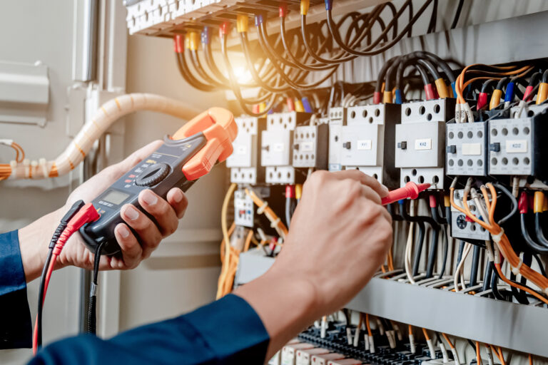 Electrician engineer uses a multimeter to test the electrical installation and power line current in an electrical system control cabinet