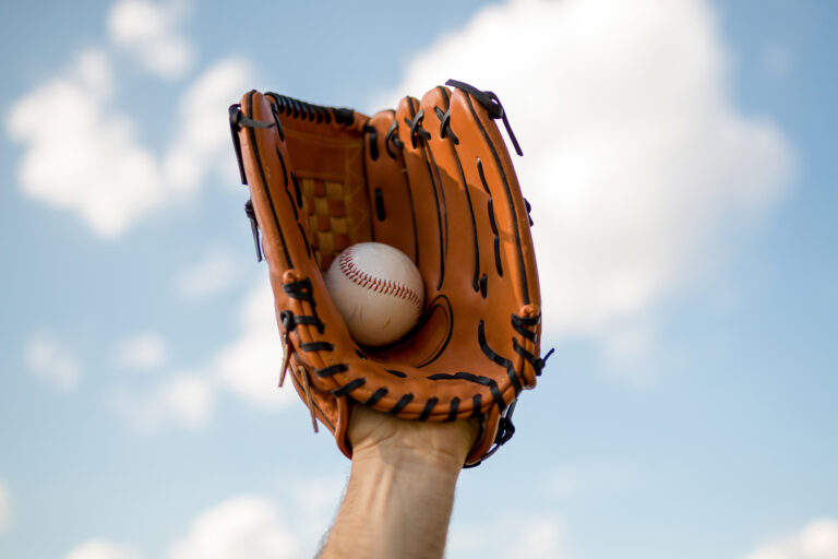 Baseball Glove catching a Baseball against a light blue sky with white clouds